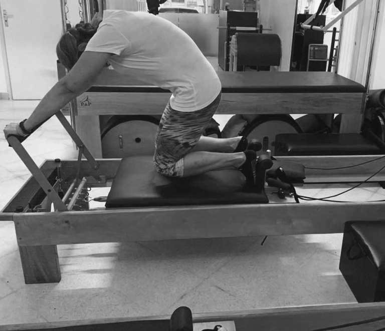 mulher realizando exercicio de variação do down stretch no reformer de pilates