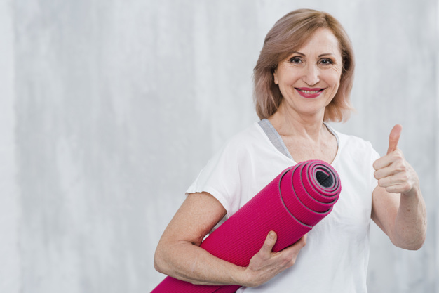 mulher de terceira idade com colchonete vermelha de pilates, realizando simbolo de ok com as mãos