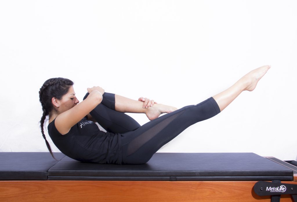 Mulher realizando exercício de pilates clássico para abdominais conhecido como The one leg stretch