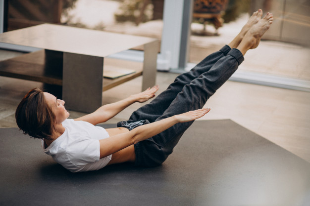 Mulher realizando exercício The Hundred de Pilates em casa